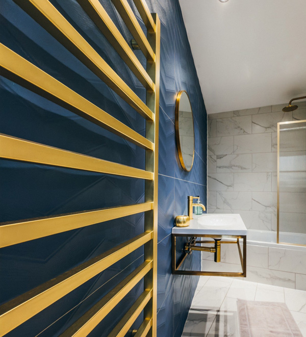 Modern bathroom with gold towel rack, blue wall, round mirror, floating sink, and white marble tiles.