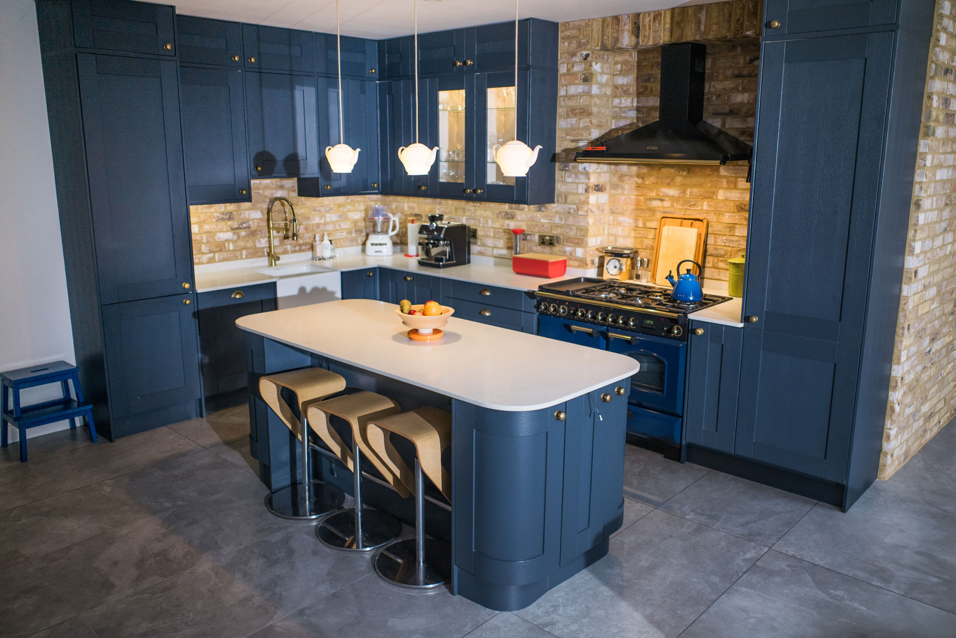 Modern kitchen with dark blue cabinets, white countertops, center island with stools, and brick backsplash.