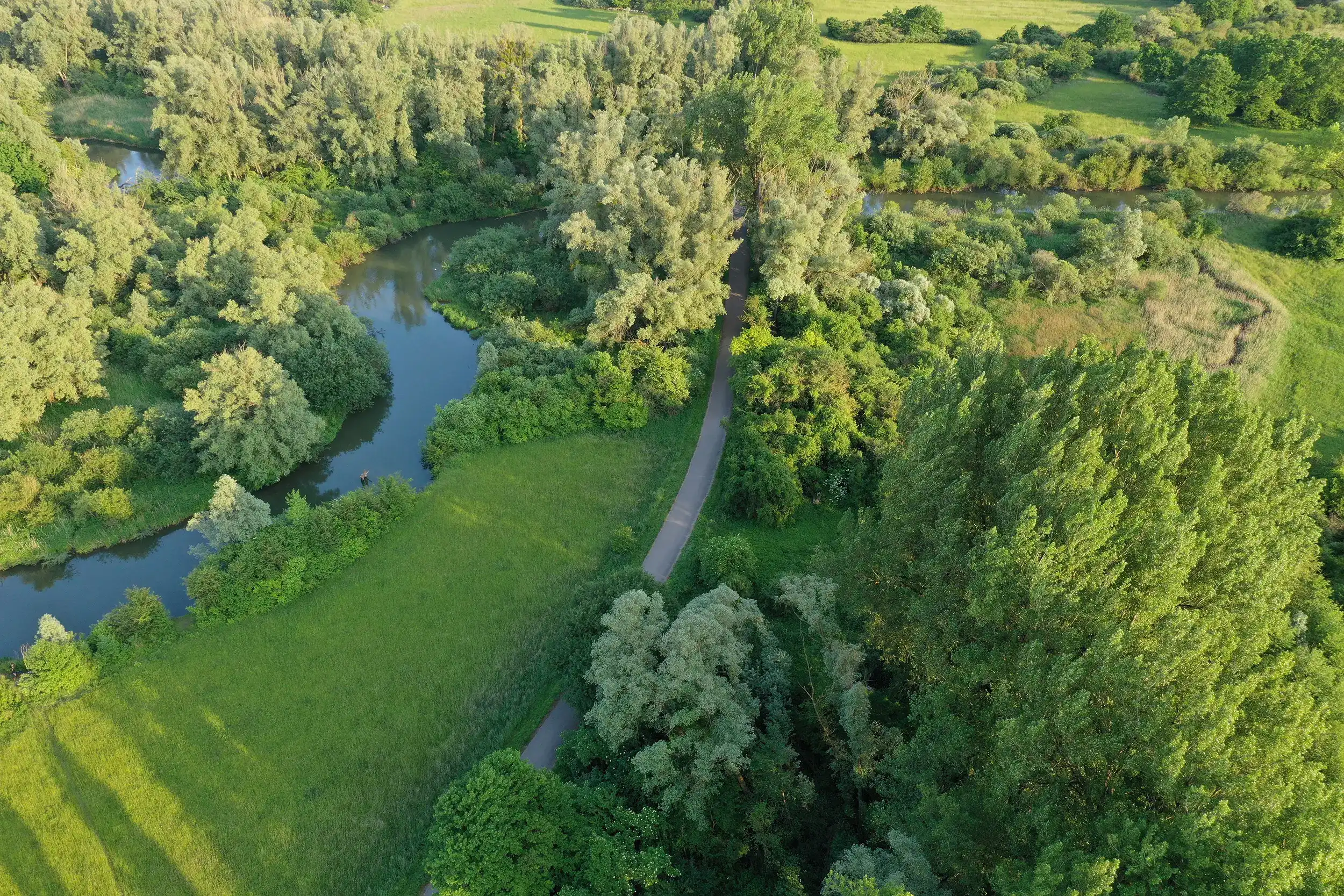 Luftaufnahme von © Patrick Pfeiffer eines Waldwegs mit Fluss und grünem Gras in einer ländlichen Landschaft.