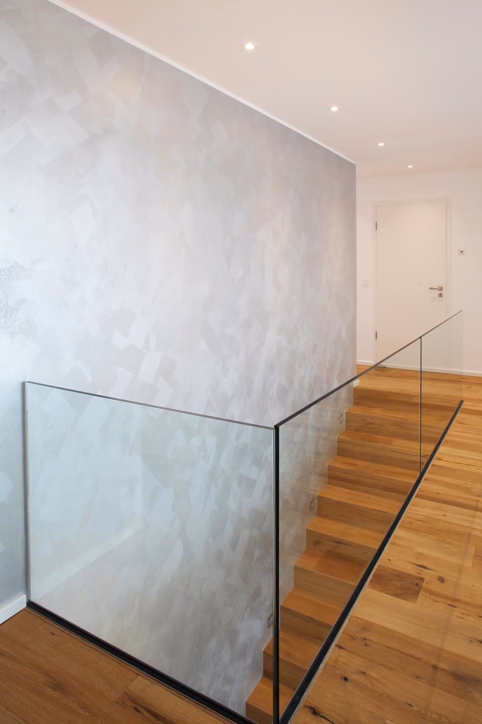 Treppenhaus mit Wand in Betonoptik und Glasgeländer