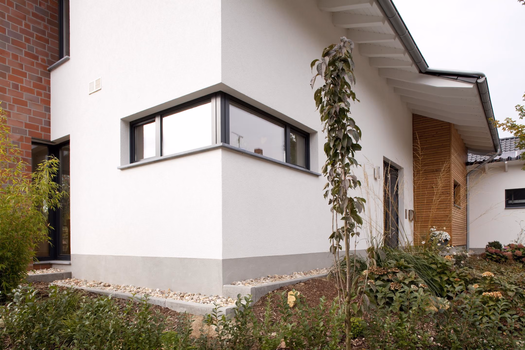 Hausecke mit Eckfenster, weißer Putzfassade und Kletterpflanze