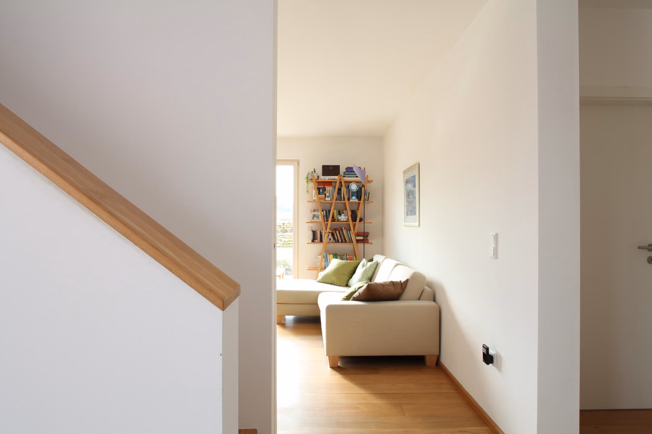 Wohnzimmer mit Sofa, Bücherregal und Blick zur Treppe