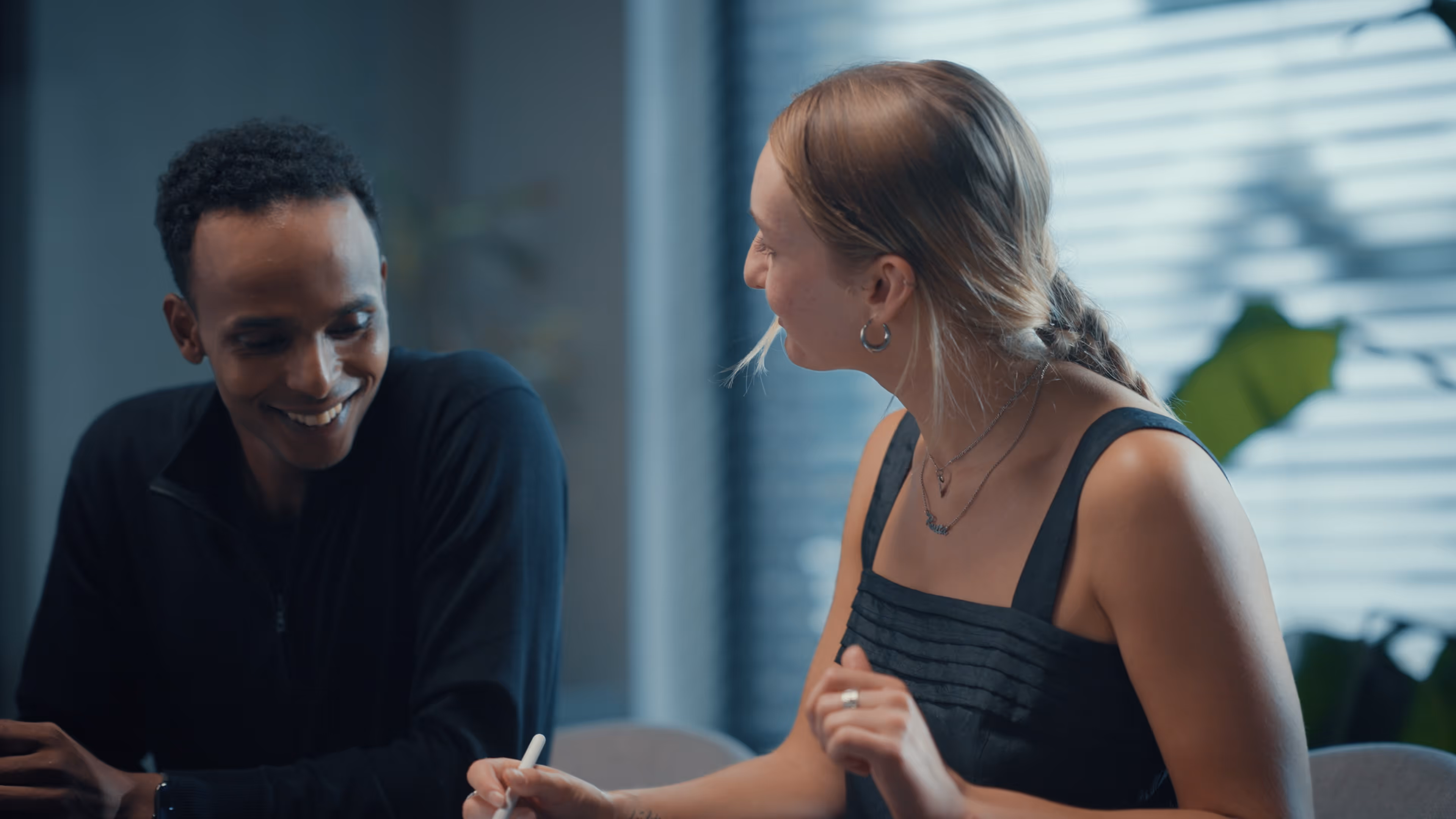 Twee mensen zitten samen en lachen terwijl ze schrijven in een lichte kamer met een raam.