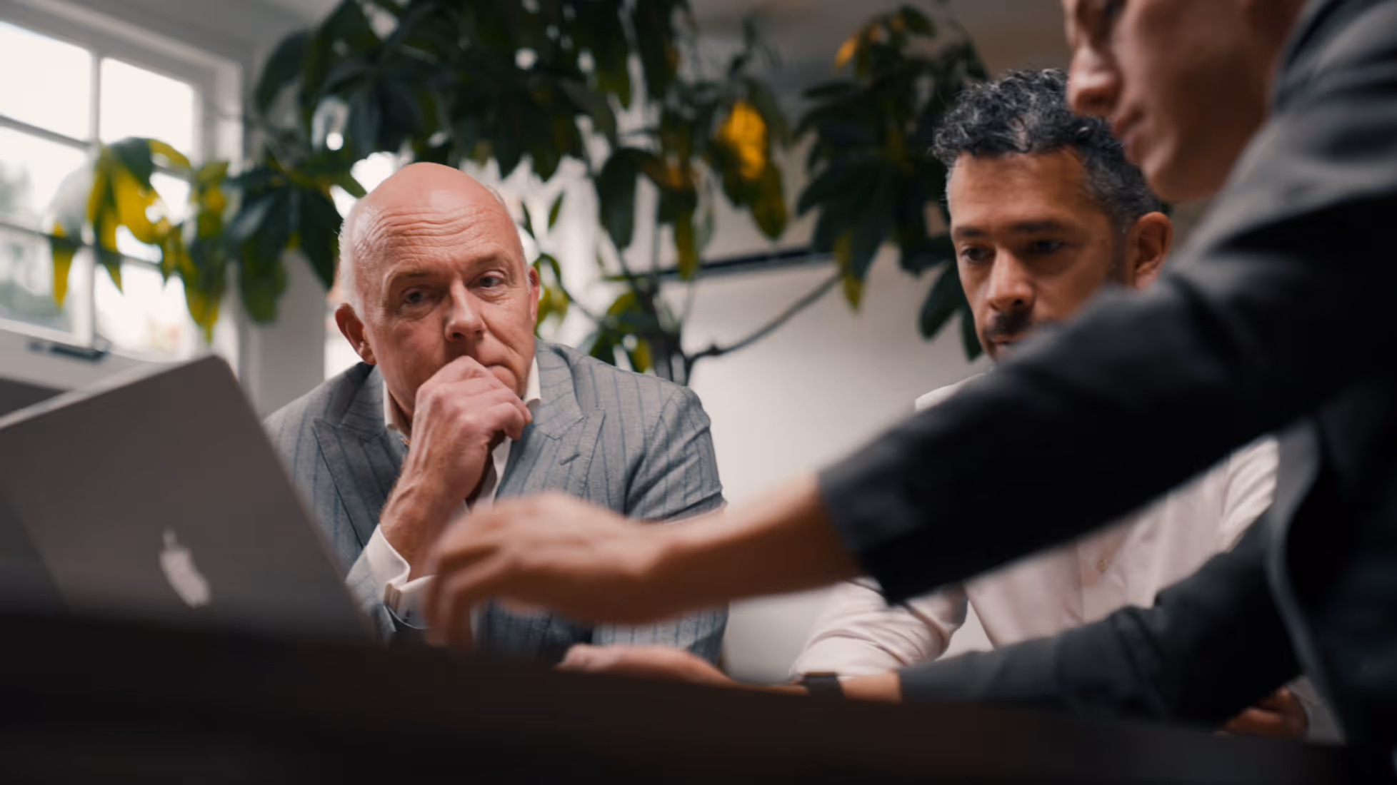 Drie mannen bespreken iets serieus terwijl ze naar een laptop kijken in een kantooromgeving.