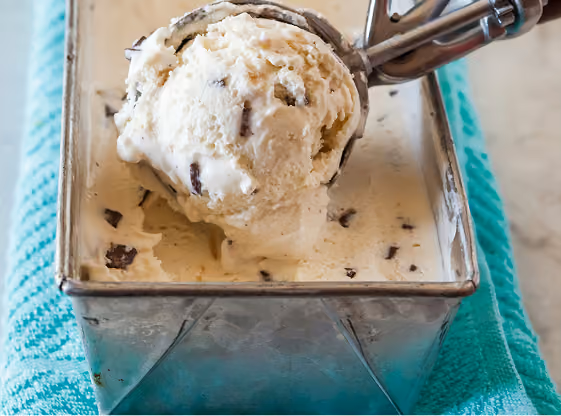 Scoop of chocolate chip ice cream being lifted from a metal container resting on a turquoise cloth.