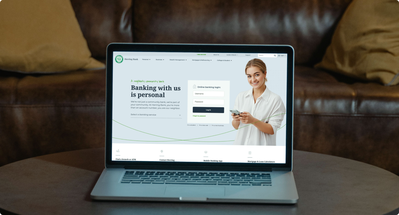 Laptop on table showing Herring Bank homepage with login form and a smiling woman holding a smartphone.