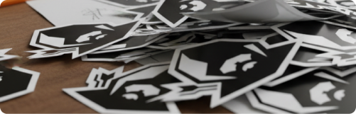 Pile of black and white stickers with a stylized face logo on a wooden surface.