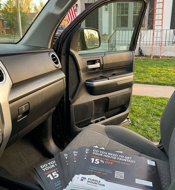Open car door with flyers on seat offering 15% off house painting by Purple Mountain Painting.