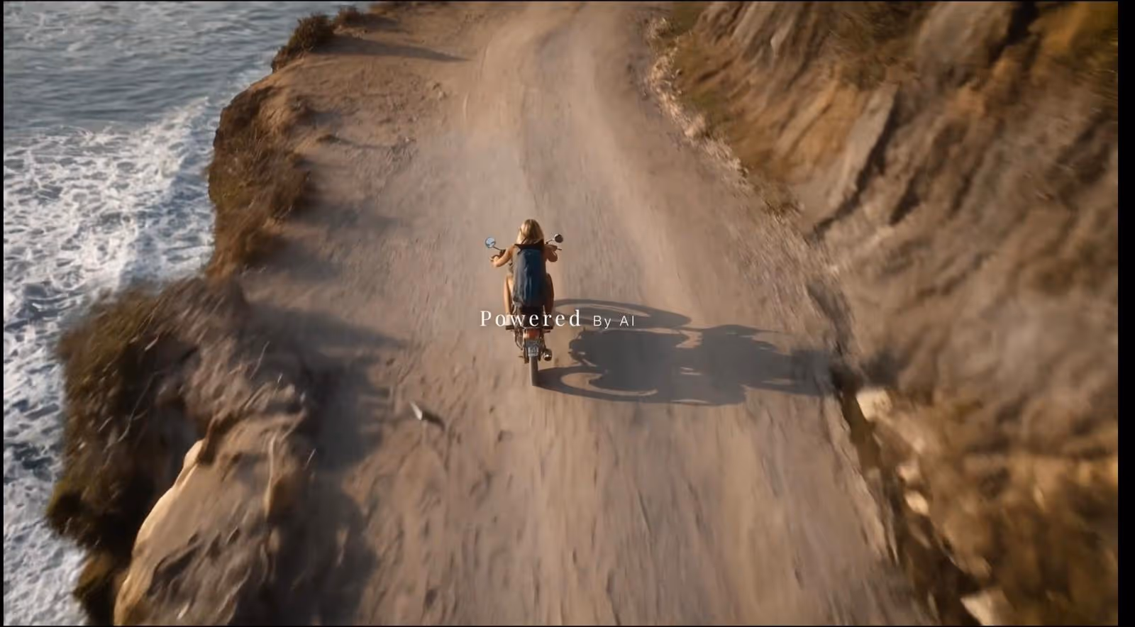 Person riding a motorcycle on a dirt road along a cliffside next to the ocean, casting a shadow on the ground.