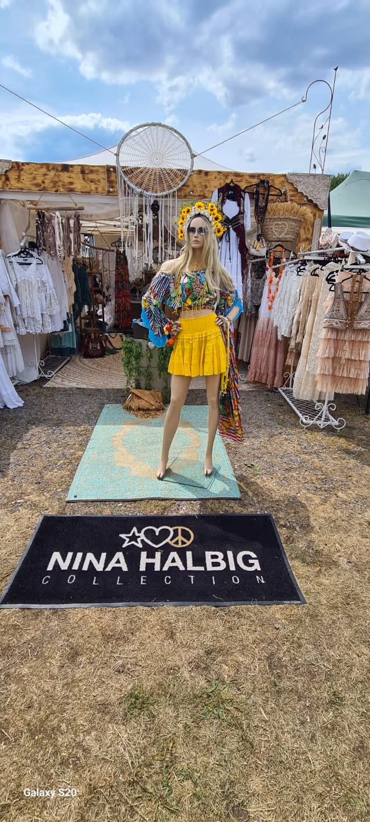 Schaufensterpuppe in buntem Top und gelbem Rock vor einem Stand mit Kleidung der Nina Halbig Kollektion.