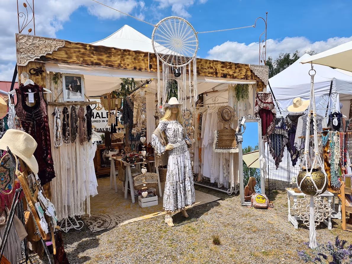 Marktstand mit Kleidung, Schmuck und Boho-Dekor bei sonnigem Wetter im Freien.