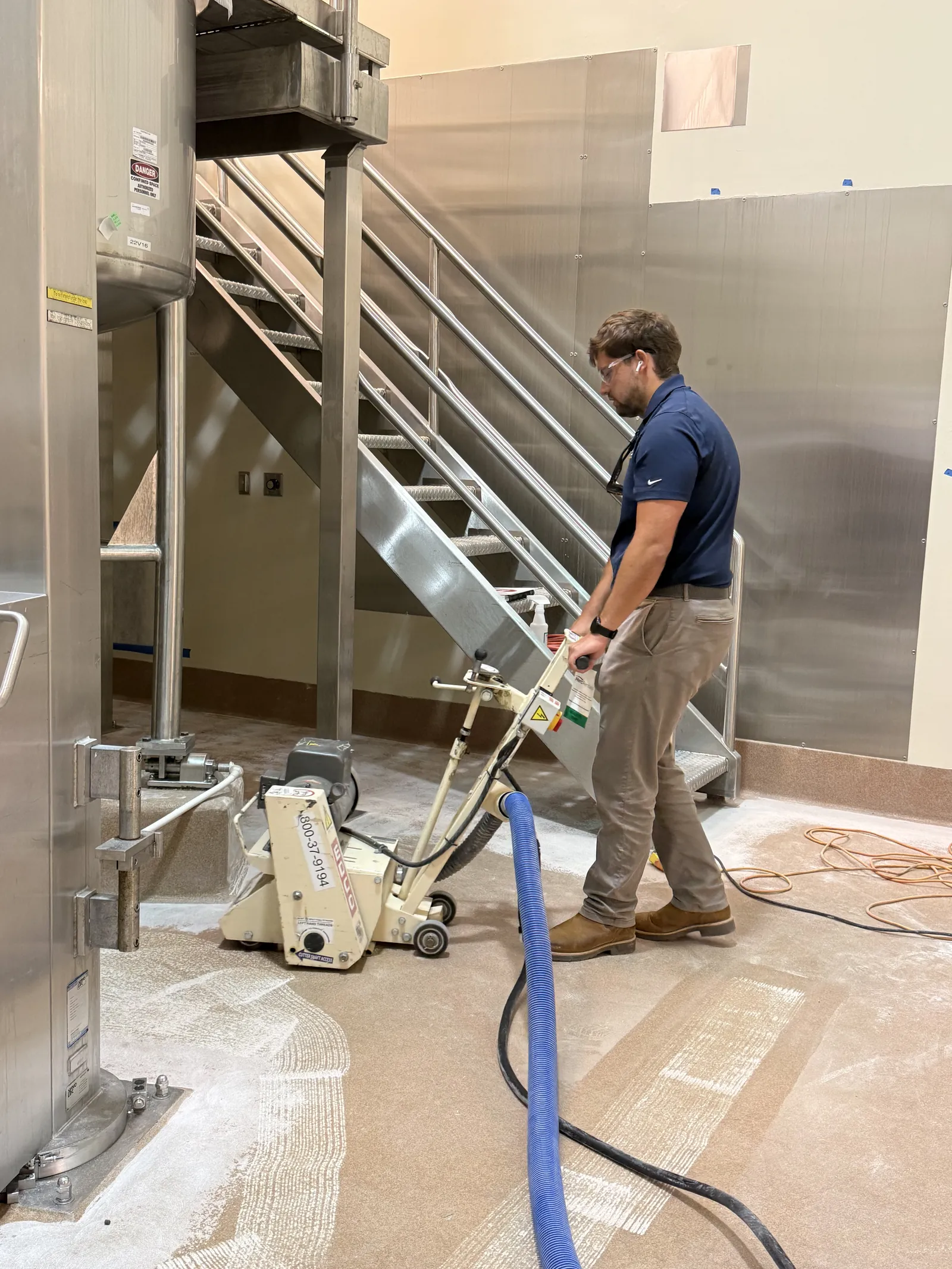 GroCo co-owner Colby Coda grinding concrete at the base of a stainless steel tank in a food processing plant
