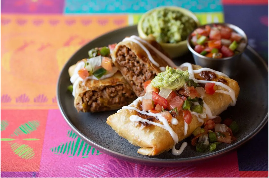 A plate with two chimichangas with guacamole on the side