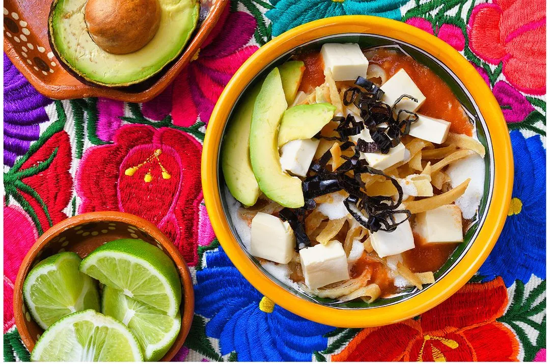 A bowl with tortilla soup and and avocado on the side
