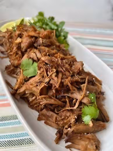 Plate of shredded cooked pork garnished with fresh cilantro and a lemon wedge on the side.