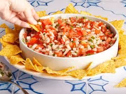 Hand dipping a tortilla chip into a bowl of pico de gallo surrounded by more chips.