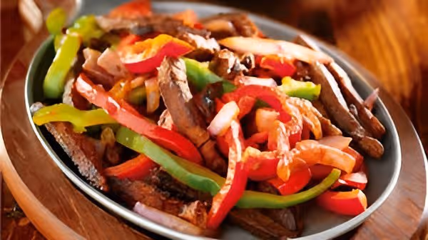Plate of grilled beef strips mixed with sautéed red and green bell peppers and onions.