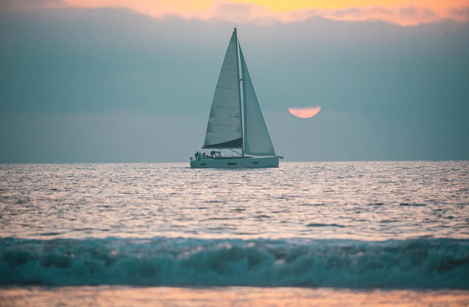 Sailboat on the open sea at sunset, with the sun low on the horizon