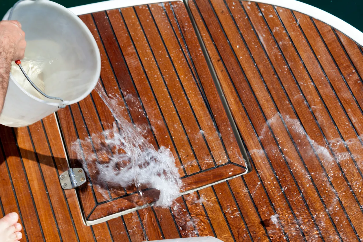 Water poured from a bucket over a wooden boat deck being scrubbed clean