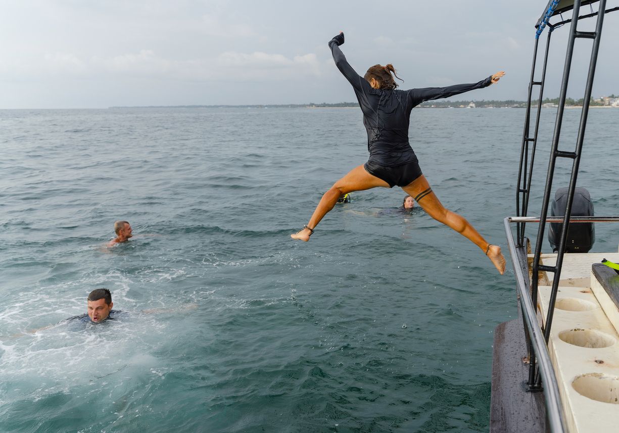 Woman leaping off the side of a boat into the sea while friends swim nearby