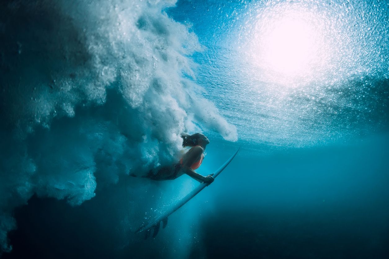 Surfer diving under a breaking wave, seen from underwater