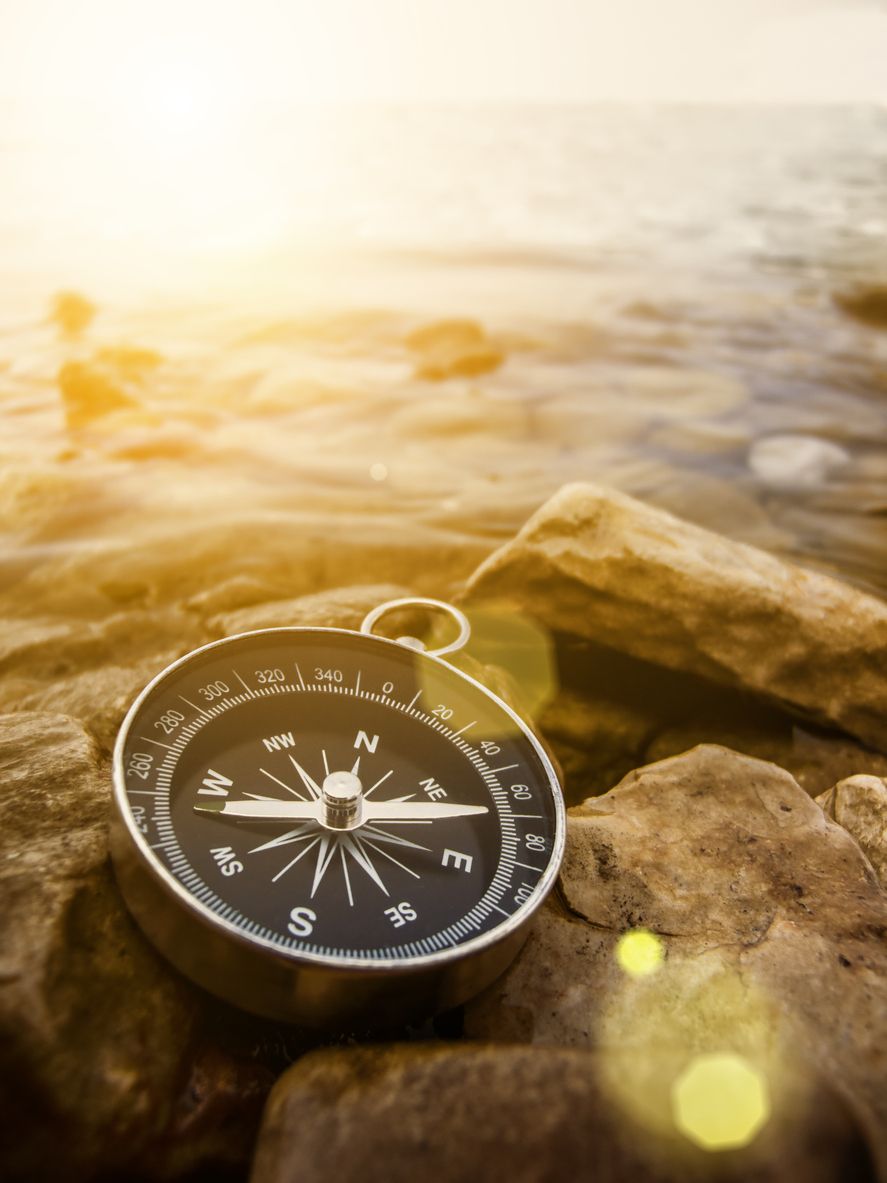 Compass resting on rocks by the water in warm sunlight