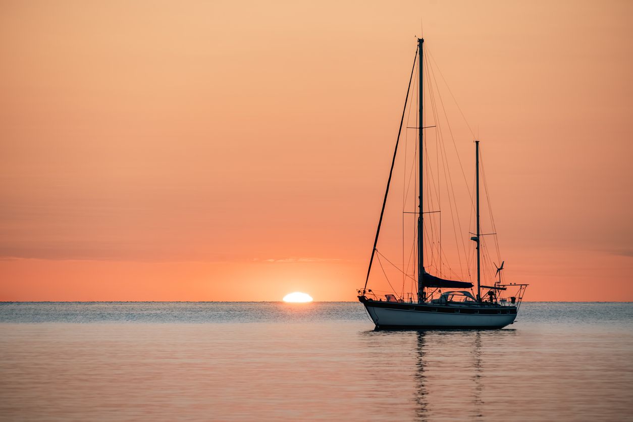 Sailboat silhouetted on calm water as the sun sets