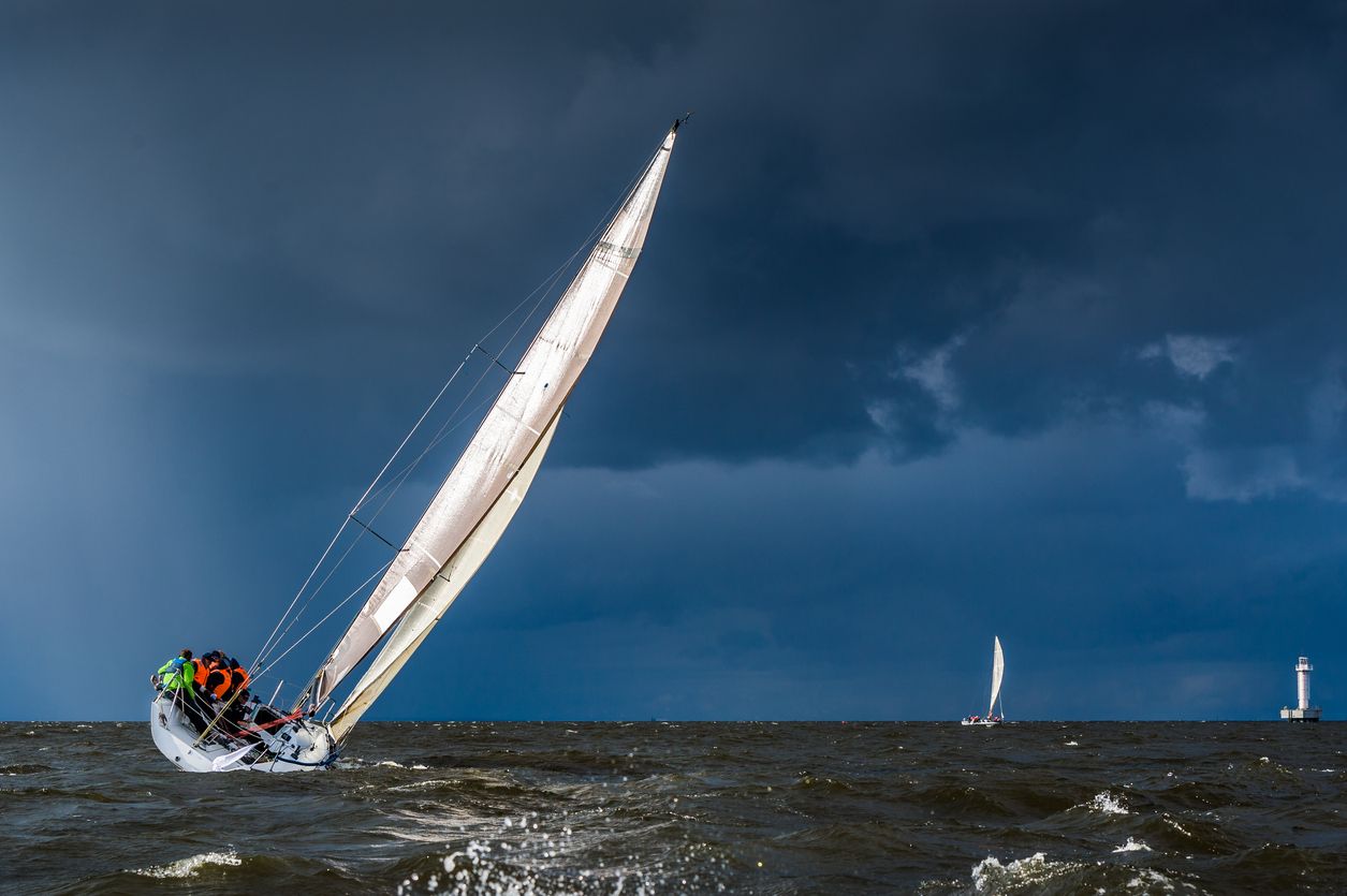 Crew leaning out on a heeling sailboat under dark storm clouds
