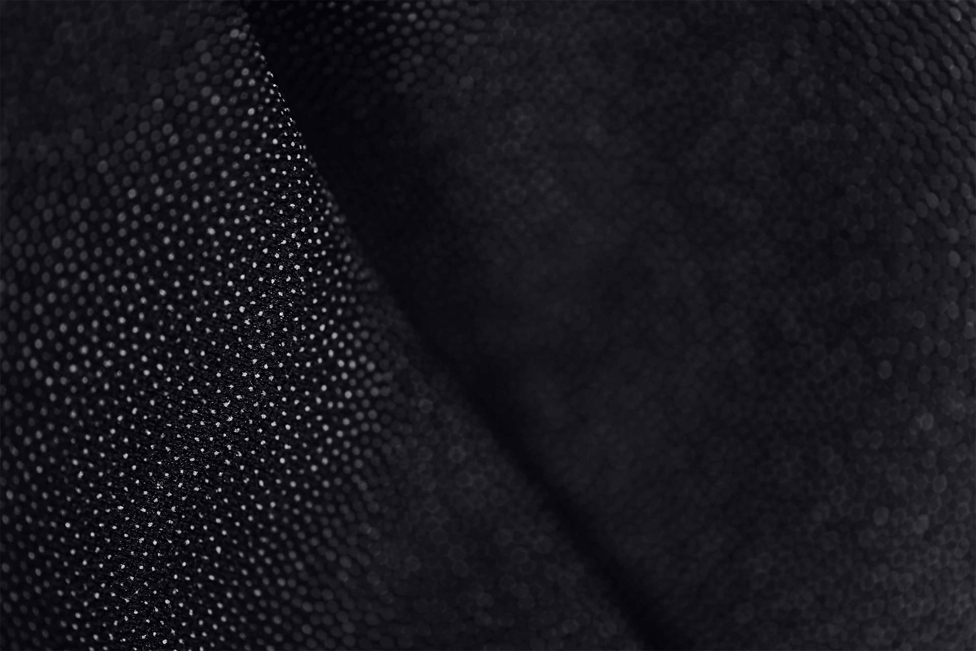 Close-up of black textured fabric with small hexagonal patterns and a slight fold.