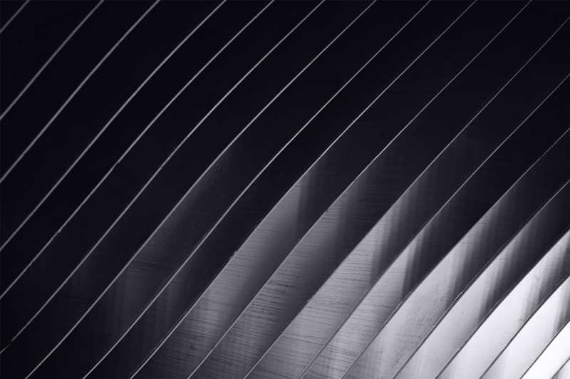Close-up of curved, overlapping black and gray slats with diagonal lines creating a pattern.
