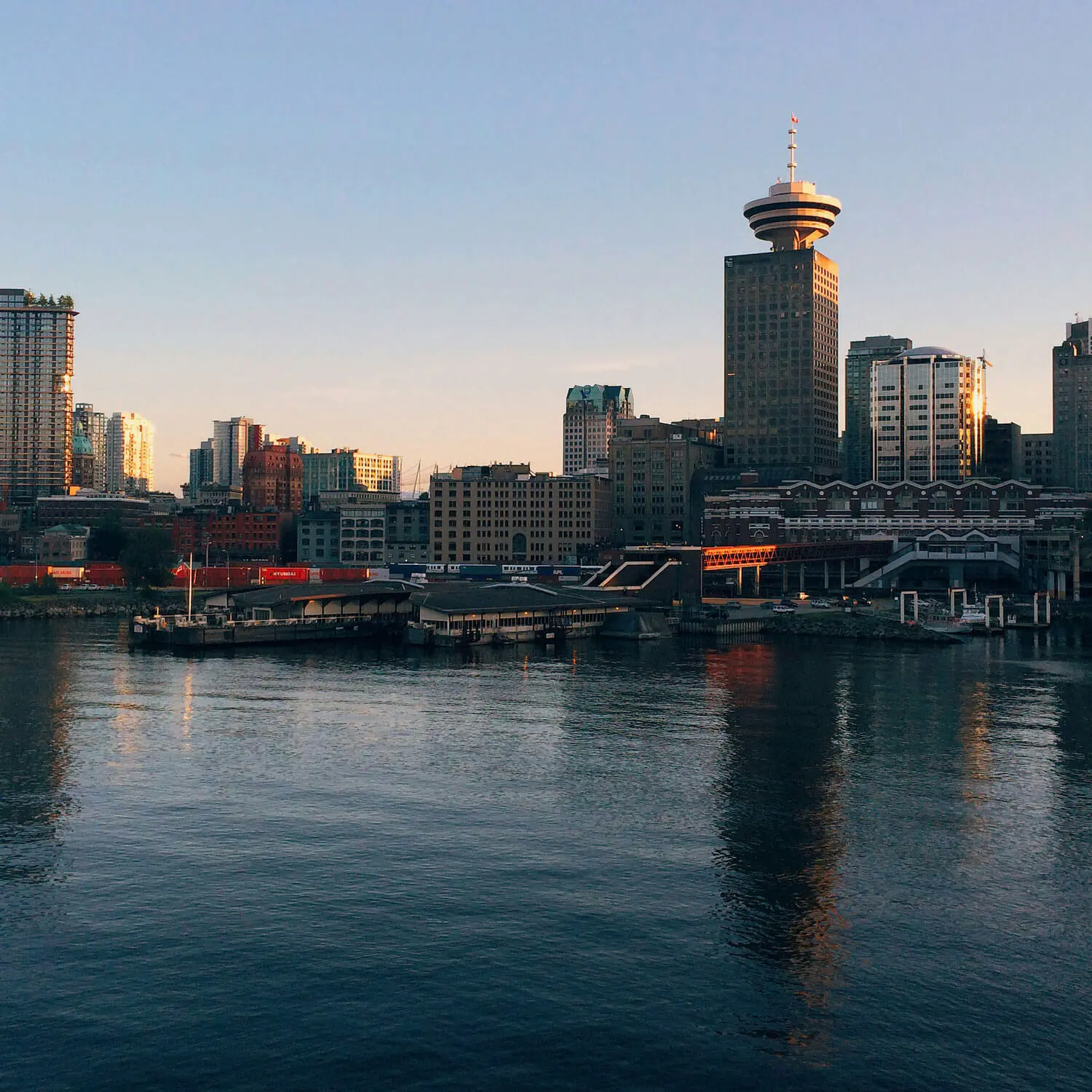 Vancouver skyline at sunset with harbor, tall tower, and modern buildings reflected in water