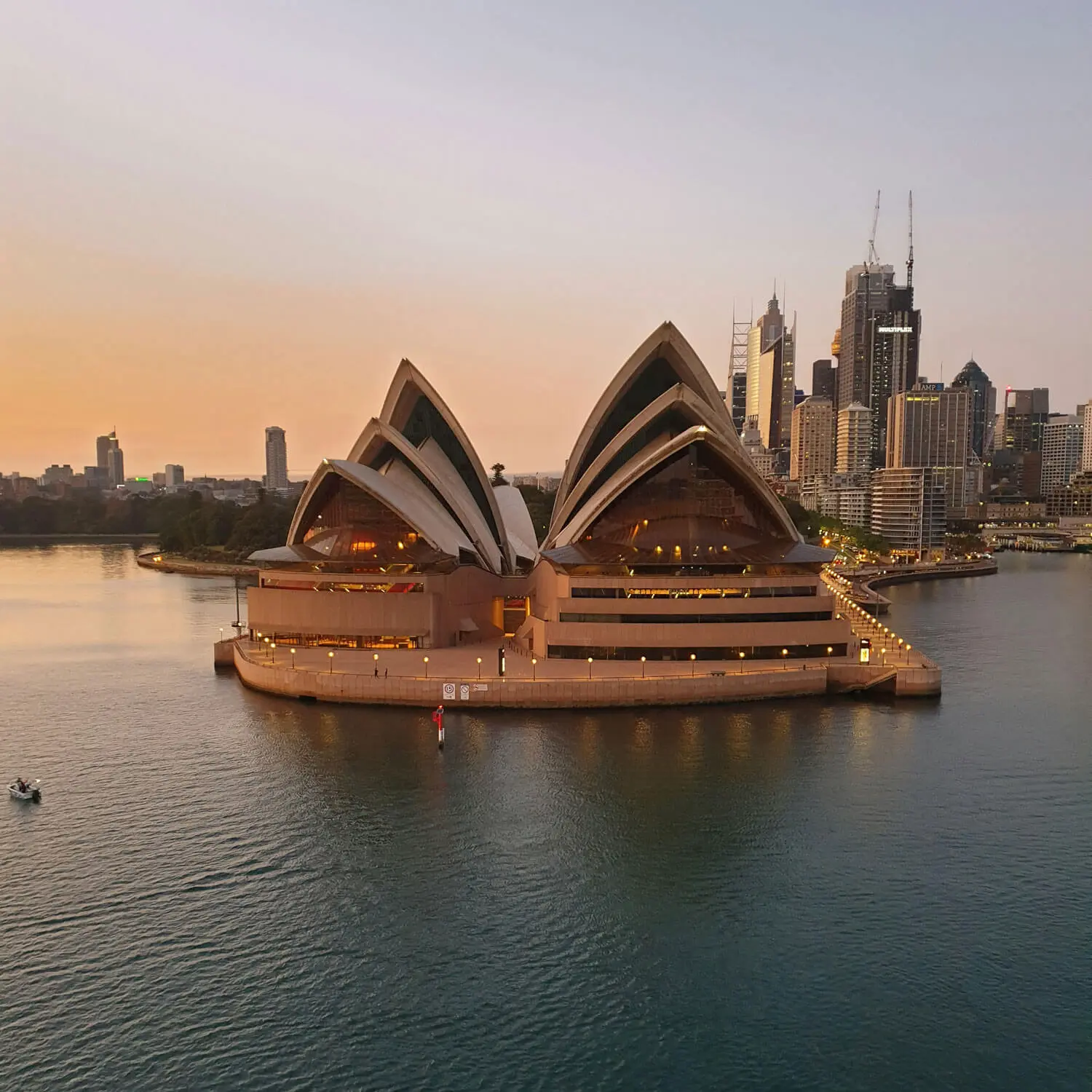 Sydney Opera House illuminated at sunset with city skyline and harbor water