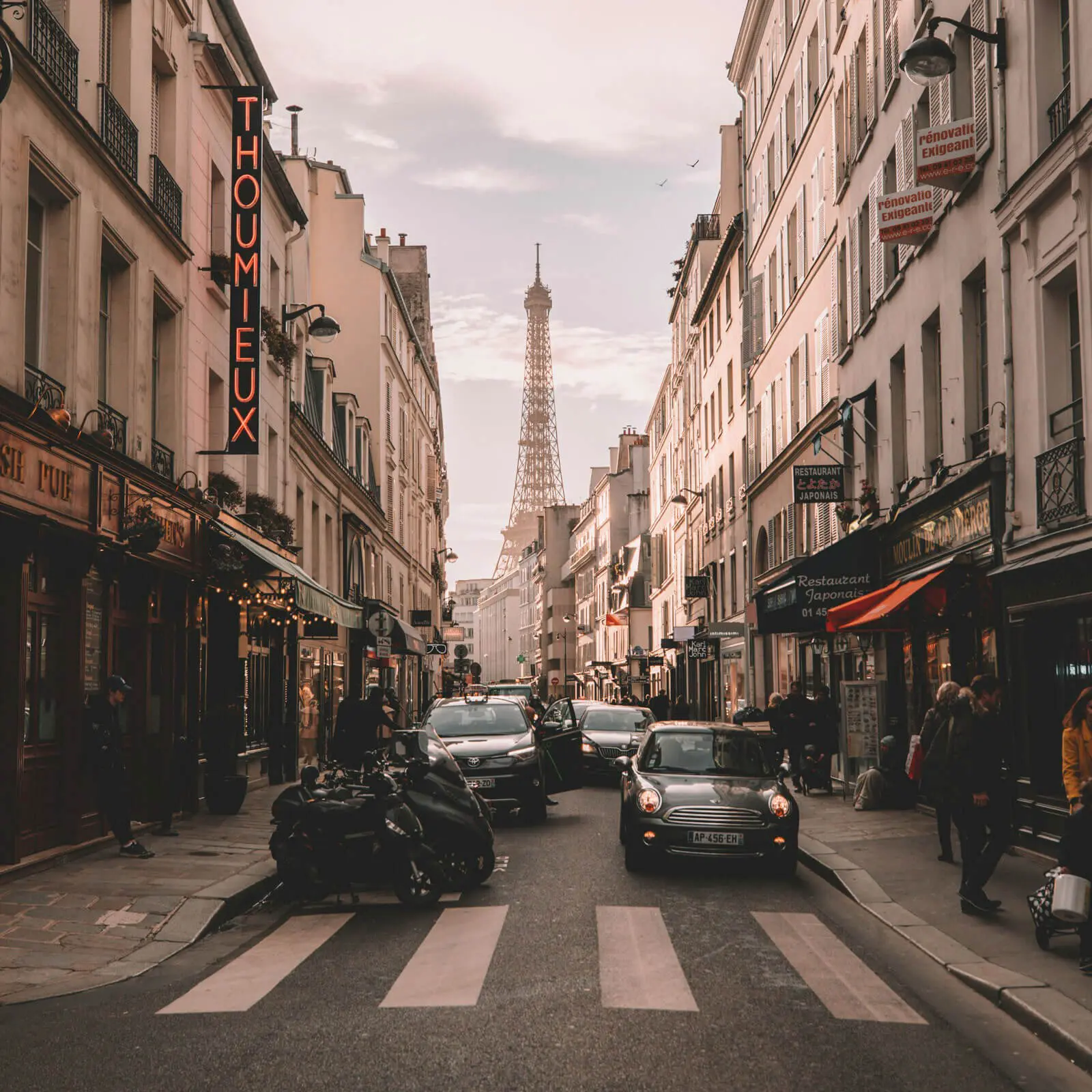 Parisian street with Eiffel Tower visible in distance, lined with shops and cafes