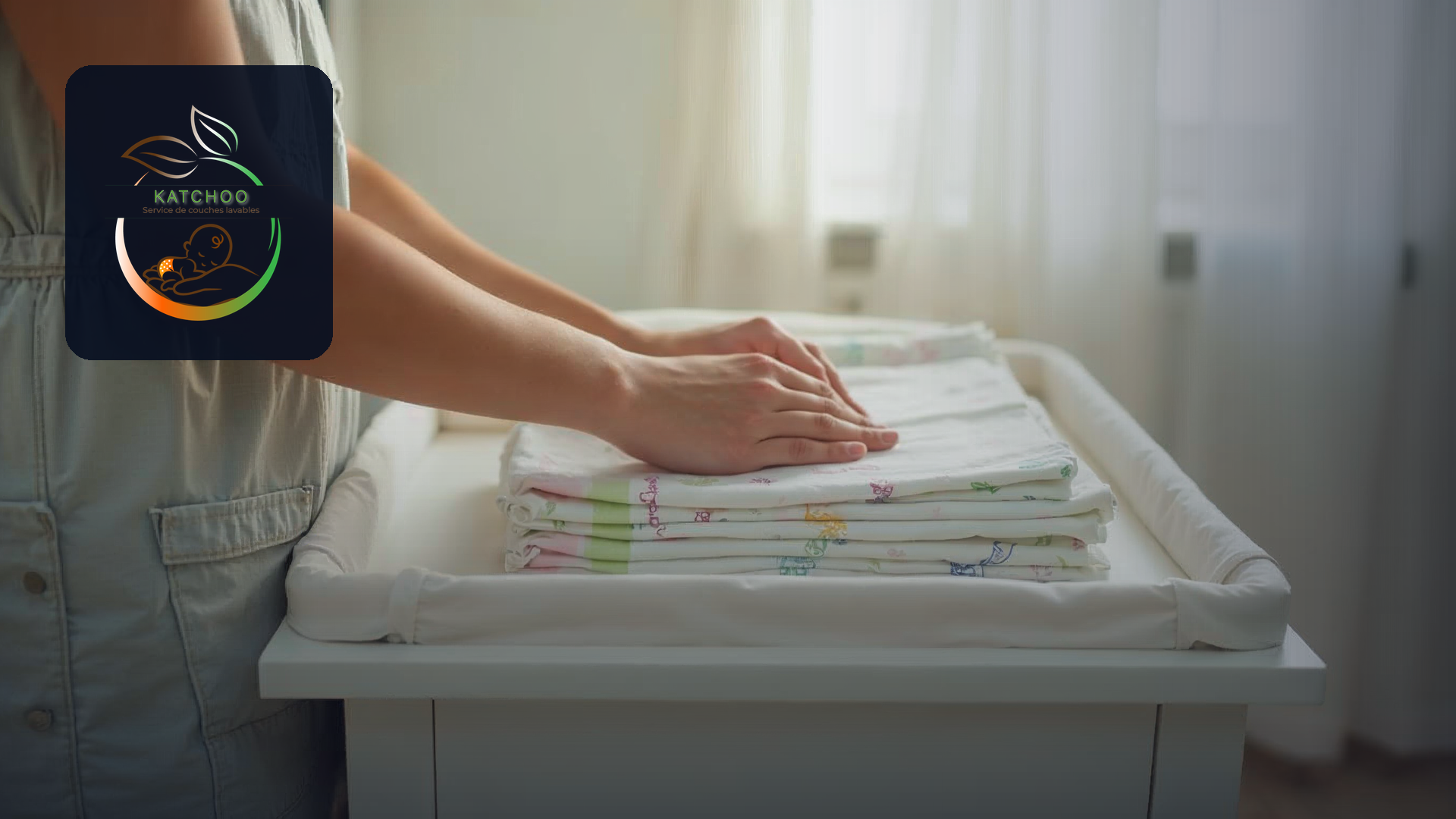 Parent folding clean cloth nappies on a nursery changing table beside a collection tote, Katchoo logo overlaid