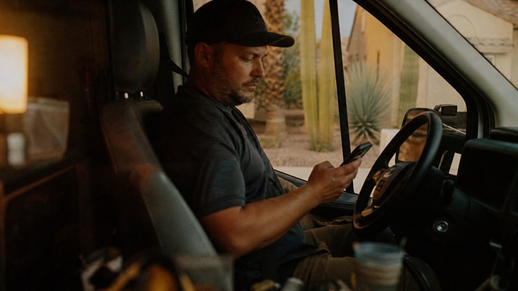 A contractor sitting in the cab of a work van reviewing a phone before driving off, photographed in Scottsdale