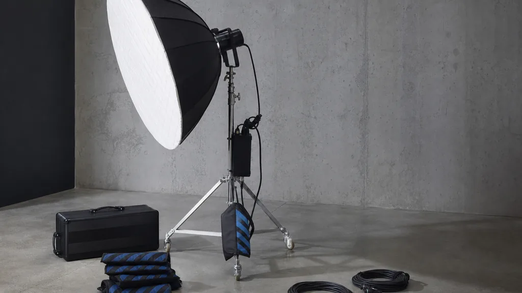 Editorial photograph of a lighting setup on a bare studio floor with a large softbox, sandbags and coiled cables