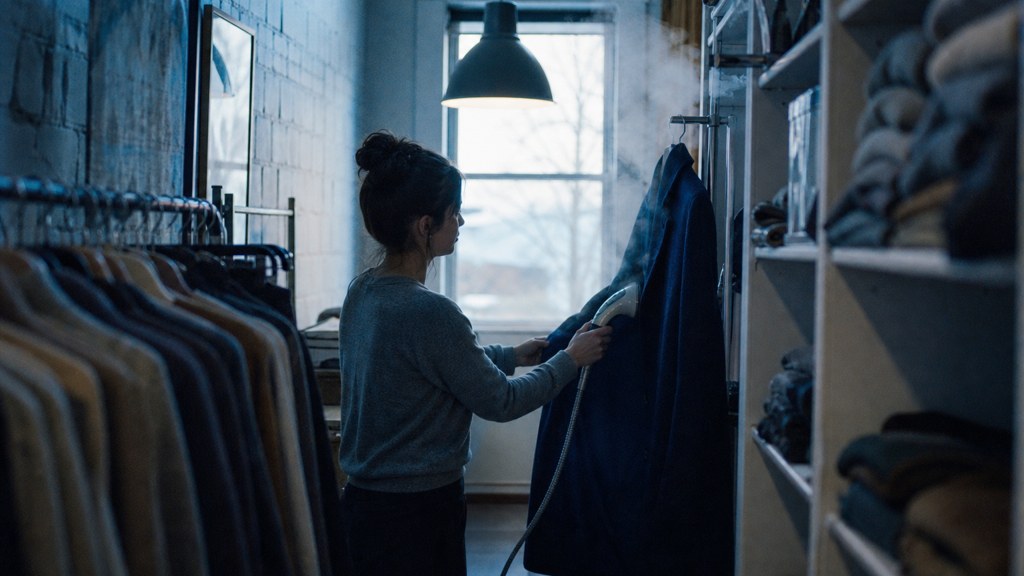 A boutique owner steaming garments in a narrow shop stockroom at opening time, photographed in Spokane