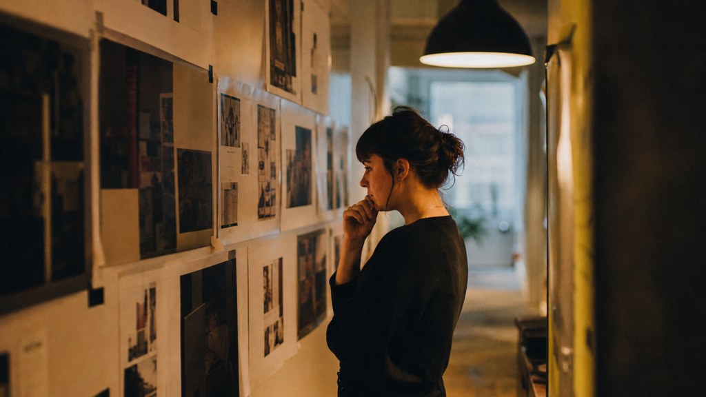 A media planner standing at a wall of printed layouts in a narrow agency corridor, photographed in Spokane