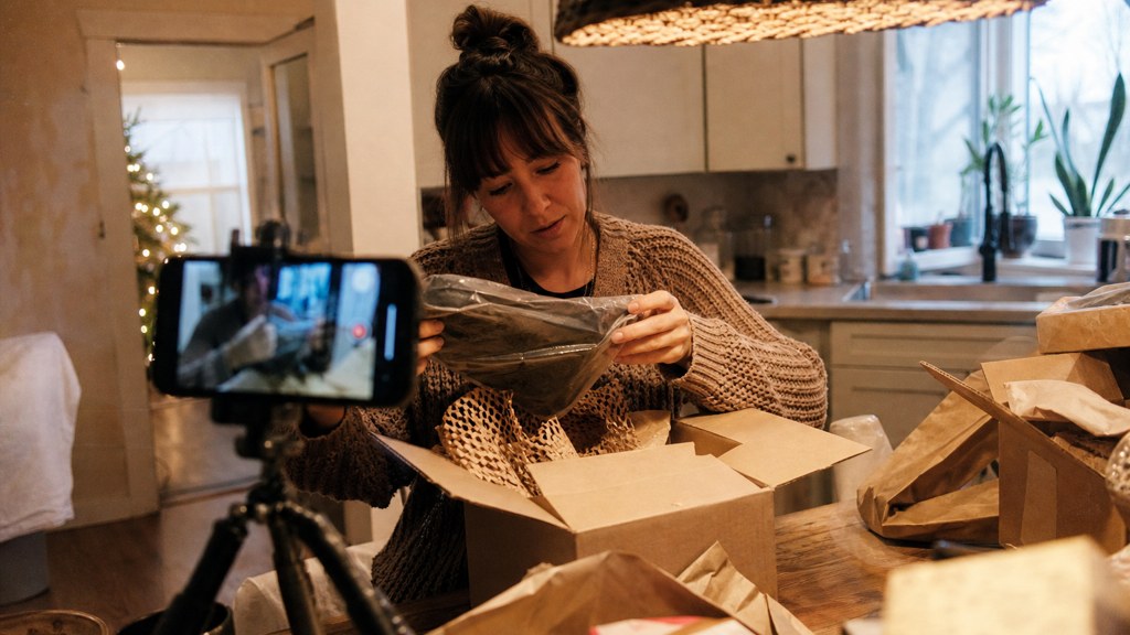 A customer filming an unboxing on a kitchen table strewn with packaging, photographed in Spokane