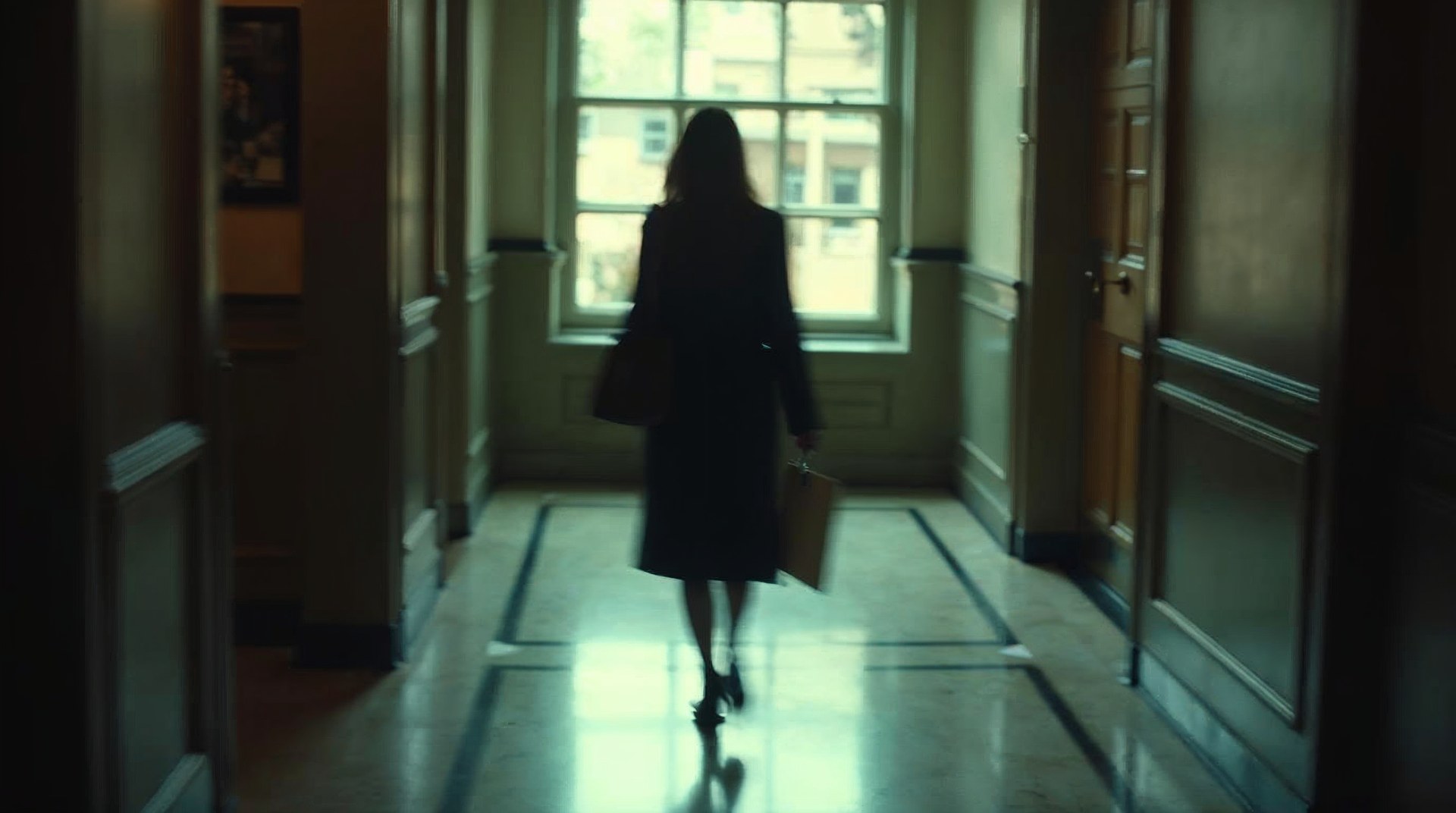 Family lawyer walking a courthouse corridor with a case file under her arm as tall window light stripes the marble floor