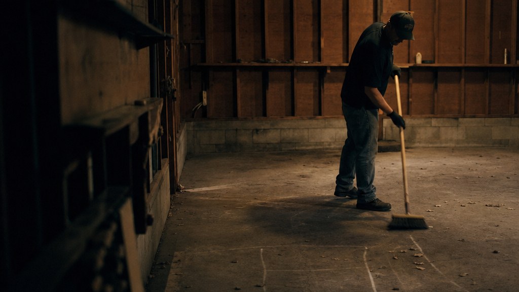 An emptied garage after an estate cleanout, one bare bulb overhead and a single worker sweeping the concrete