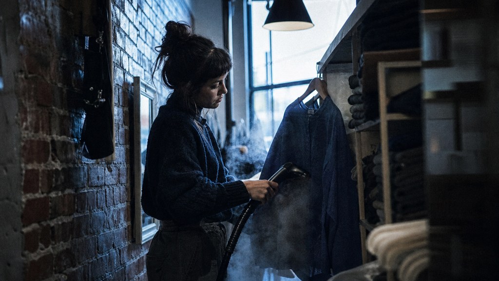A boutique owner steaming garments in a narrow shop stockroom at opening time, photographed in Tulsa