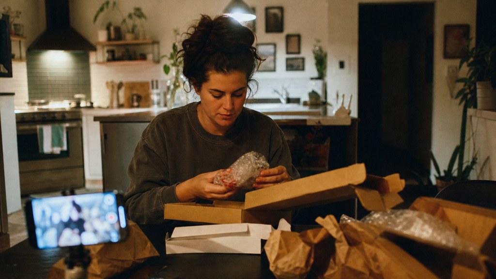 A customer filming an unboxing on a kitchen table strewn with packaging, photographed in Tulsa