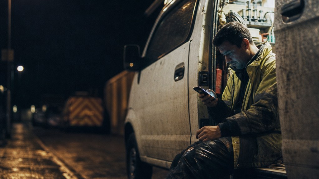 Technician checking his phone in the open door of a restoration van at night under a streetlight