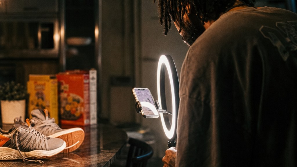 Creator filming a pair of running shoes on a kitchen counter with a ring light and a cracked phone clamp