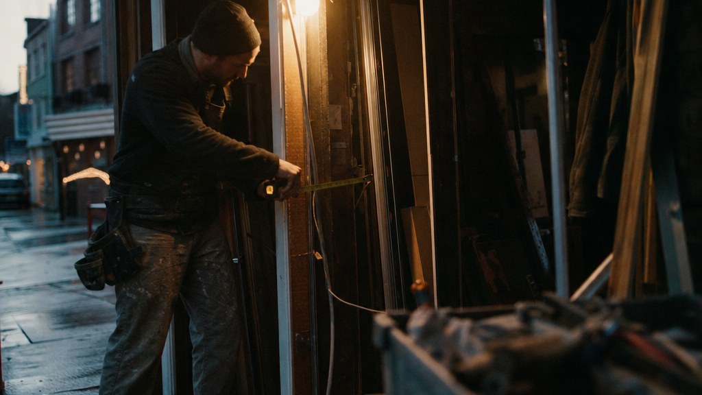 Builder measuring a shop doorway with a steel tape at dawn with dust in the light shaft