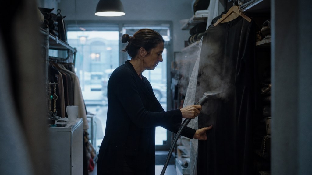 A boutique owner steaming garments in a narrow shop stockroom at opening time, photographed in Virginia Beach