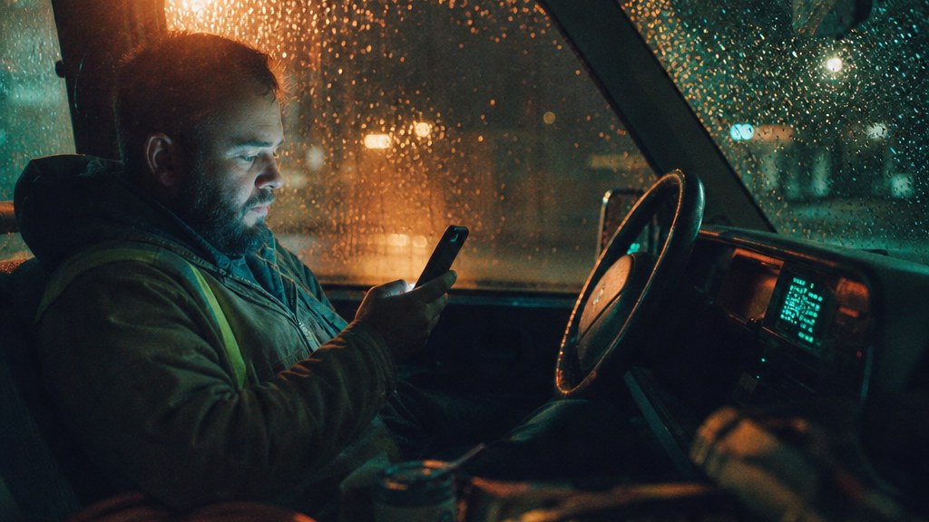 Electrical contractor reading an assistant answer on his phone in a parked truck in the rain