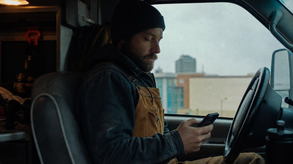 A contractor sitting in the cab of a work van reviewing a phone before driving off, photographed in Wichita