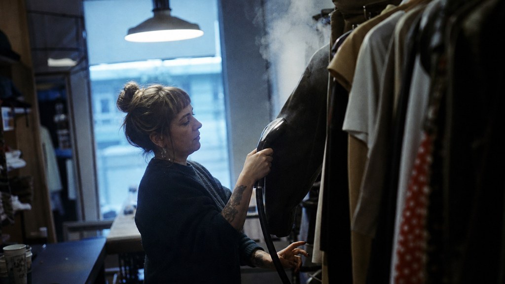 A boutique owner steaming garments in a narrow shop stockroom at opening time, photographed in Wichita